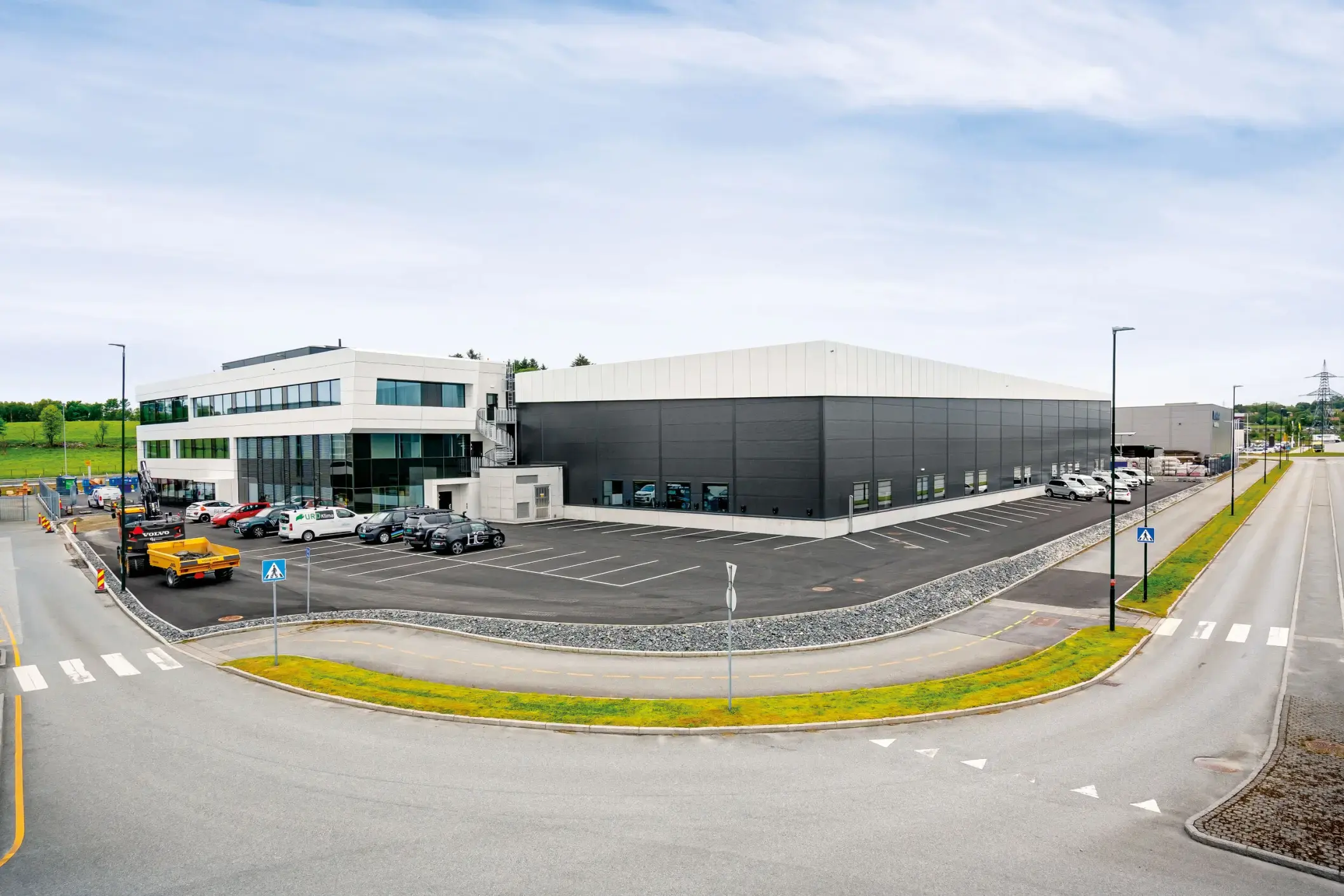 Kombinasjonsbygg med kontordel og en stor hall med flatt tak, sett fra veien