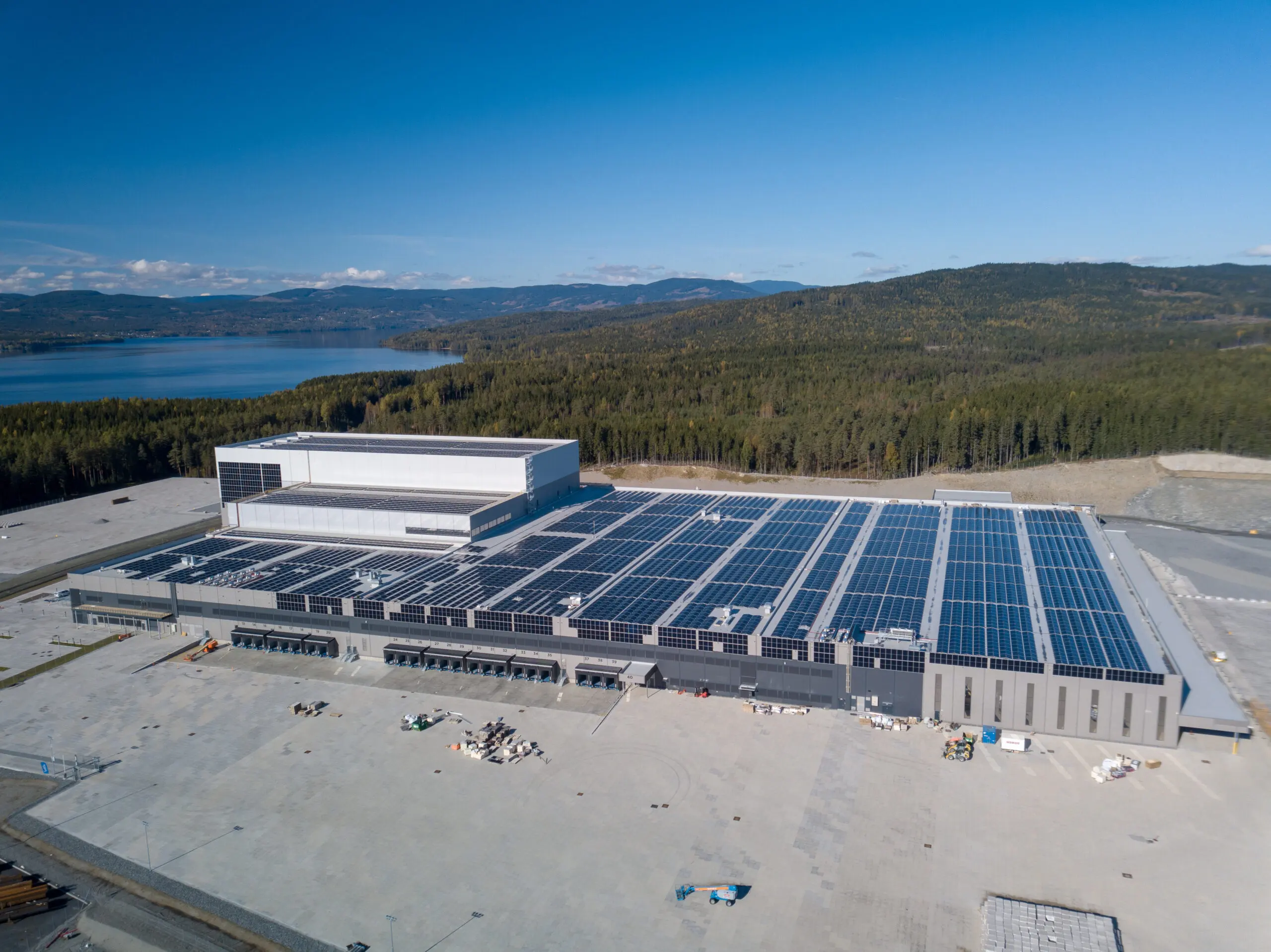 Logistikksenter med solcellepaneler over store deler av taket, med fjord og skog i bakgrunnen